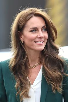 a woman with long hair wearing a green blazer and white shirt smiles at the camera