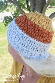 a woman wearing a multicolored crocheted hat in front of a tree