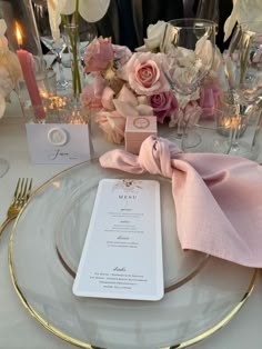 the table is set with pink and white flowers, silverware, and menu cards