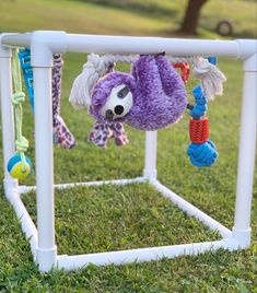 a purple stuffed animal hanging from a white frame in the grass next to a tree