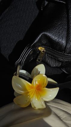 a yellow flower sitting on top of a black leather bag next to it's zipper