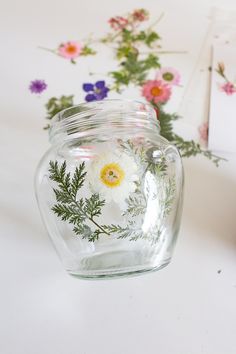 a glass jar filled with flowers on top of a white table next to a card