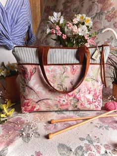 a pink floral purse sitting on top of a table next to flowers and knitting needles