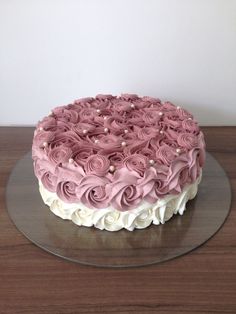 a cake with pink frosting and white flowers on a glass plate sitting on a wooden table