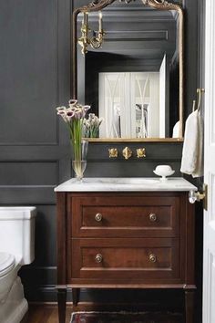 a white toilet sitting next to a bathroom sink under a mirror on top of a wooden cabinet