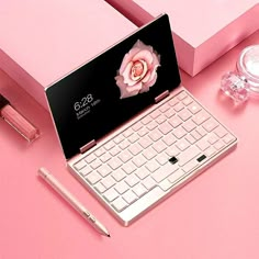 an open laptop computer sitting on top of a pink desk next to a bottle of perfume