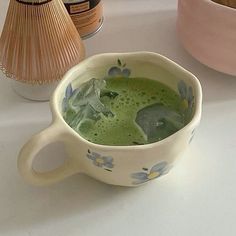 a cup filled with green liquid sitting on top of a table next to vases