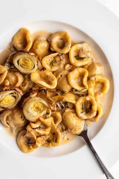 a white plate filled with pasta and artichokes on top of a table