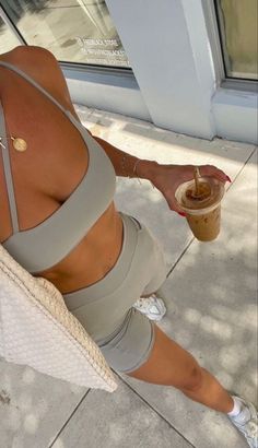 a woman in grey sports bra and shorts holding a cup of coffee on the sidewalk