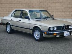 an old bmw is parked in front of a brick wall on the side of the road