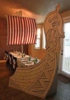 a long table with plates and wine glasses on it in front of a large paper boat