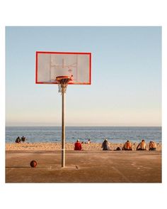 a basketball hoop on the beach with people sitting in the sand