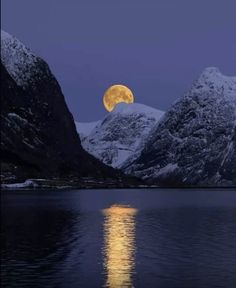 the full moon is reflected in the still water of a lake with snow covered mountains behind it