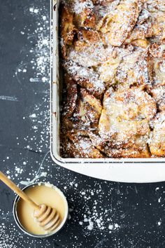 a baking dish with powdered sugar on top and a spoon in the bowl next to it