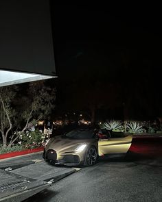 a silver and gold sports car parked in front of a building at night with lights on