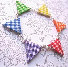 four different colored triangles are hanging from a silver chain on a flowery surface with flowers in the background