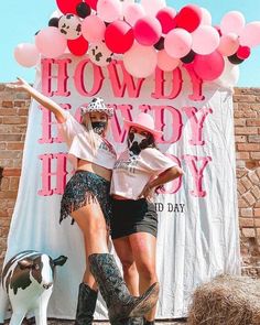 two women standing in front of a sign with balloons and cowgirls on it