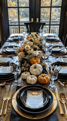 a table set with black and white plates, silverware and pumpkins on it