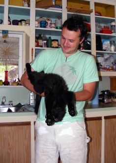 a man holding a black cat in his hands while standing next to a kitchen counter