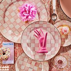 a table topped with plates covered in pink and white checkerboard design, doughnuts and flowers