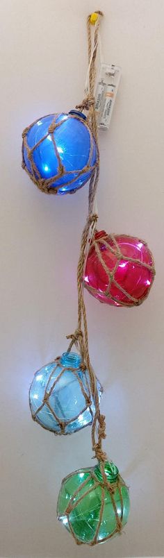 three colorful glass ornaments hanging from twine with string on white wall and light background