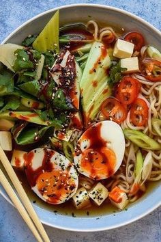 a bowl filled with noodles and vegetables next to chopsticks on a blue surface