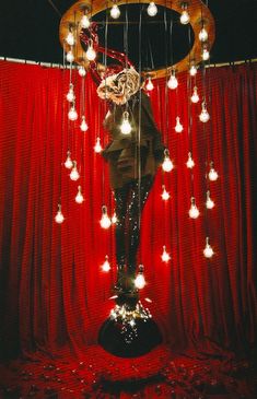 a statue with many lights hanging from it's sides in front of a red curtain