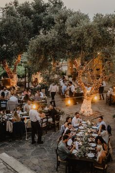 a group of people sitting at tables in the middle of an outdoor area with trees and lights