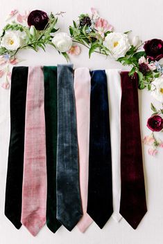 five ties laid out on top of each other in different colors and designs with flowers around them