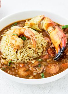 a bowl filled with shrimp and rice on top of a white table next to a cup