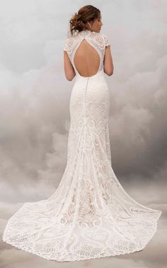 a woman in a white wedding dress looking back at the camera with clouds behind her