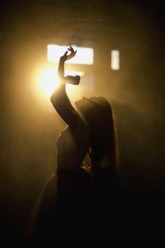 a woman holding her hand up in the air at night with light coming from behind