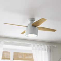 a white ceiling fan with wooden blades in a living room next to a large window