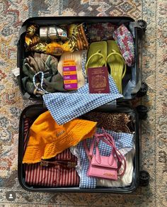 an open suitcase filled with clothes and other items on the floor next to a rug