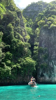 two people on a boat in the water near some cliffs and trees with green foliage