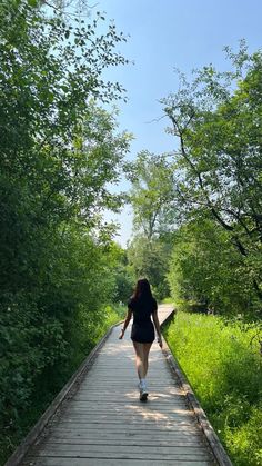 a woman walking down a wooden walkway in the middle of some green grass and trees