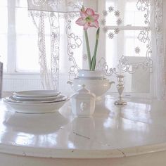 a white table topped with plates and vases filled with flowers next to a window