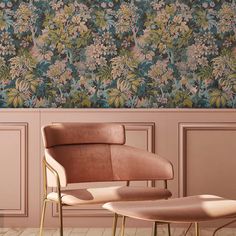 a chair and foot stool in front of a wall with floral wallpaper on it