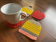 three crocheted coasters and a coffee cup on a wooden table with a white mug in the middle