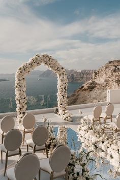 an outdoor ceremony setup with white flowers and chairs on the ground, overlooking the ocean