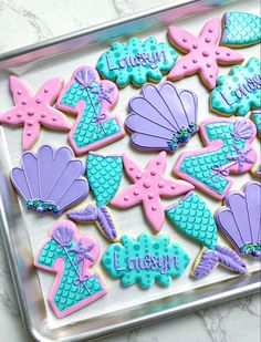 decorated cookies in the shape of little mermaids on a tray with name written on them