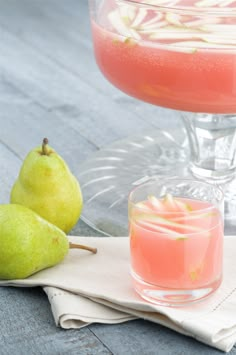 two pears are sitting on a napkin next to a glass of watermelon juice