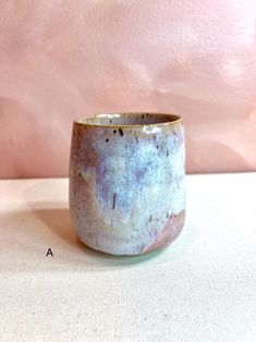 a white and blue cup sitting on top of a table next to a pink wall