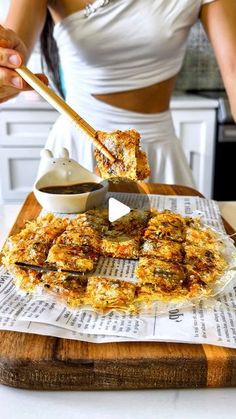 a woman cutting up food on top of a wooden cutting board with chopsticks