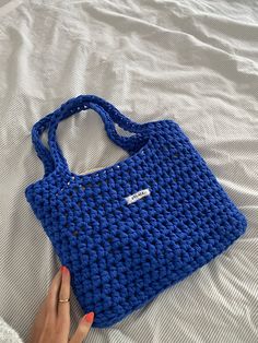 a woman's hand holding a blue crocheted purse on top of a bed