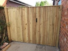 a wooden gate in front of a brick wall next to a sidewalk and fenced yard