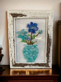 a vase with blue flowers in it sitting on a table next to a wall hanging