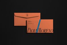 two orange envelopes sitting next to each other on top of a black surface with the word poli moreno printed on it