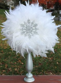 a silver vase with white feathers and a snowflake decoration on the top in front of some grass