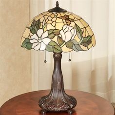 a table lamp with flowers on it sitting on top of a wooden table next to a window